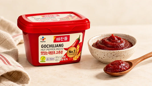 CJ Haechandle Gochujang 500g tub beside a bowl and spoon of Korean hot pepper paste