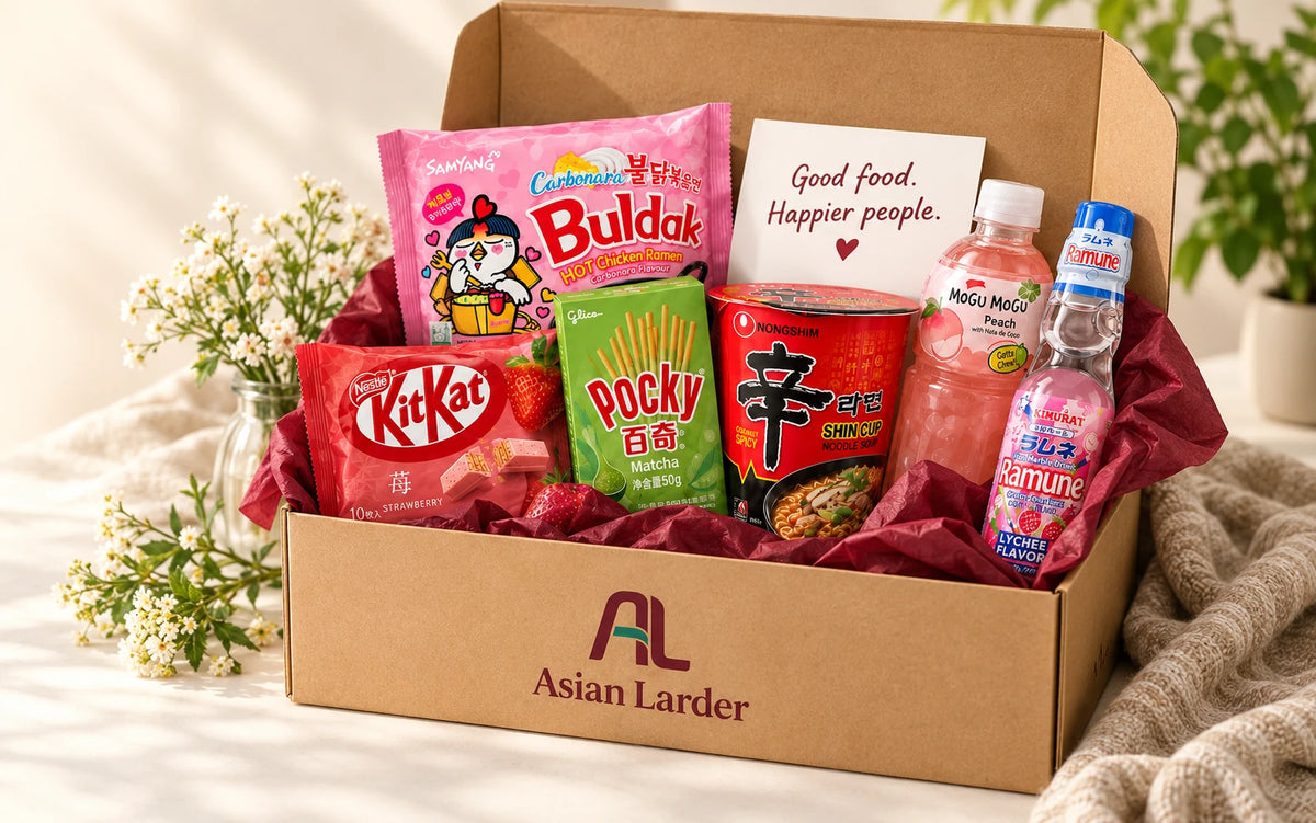 An open Asian Larder gift box with Asian snacks, drinks, burgundy tissue and a Good food. Happier people. note